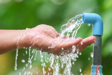 Mavi bir musluktan ellere akan suyun yakın çekimi açık hava ortamında tazeliği ve sürdürülebilirliği sembolize ediyor..