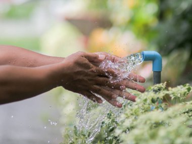 Adam bahçe fıskiyesiyle su püskürtüyor.