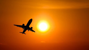 Canlı turuncu bir günbatımı gökyüzünde süzülen bir uçağın silueti seyahat, özgürlük ve macerayı simgeliyor..