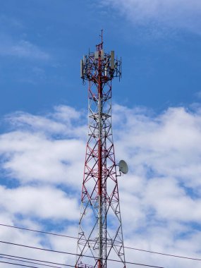 Kabarık beyaz bulutlarla çevrili, parlak mavi bir gökyüzüne uzanan yüksek bir iletişim yapısı..