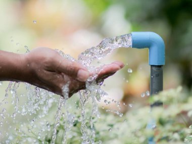 Mavi bir musluktan akan suyun yakın plan görüntüsü yeşillik ve sürdürülebilirliği sembolize ediyor..