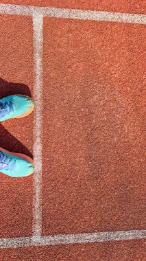 Beyaz çizgileri olan kırmızı koşu pistinde mavi spor ayakkabıları, spor ve fitness temaları için mükemmel..