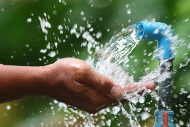 Mavi bir musluktan taze su yakalayan eller, saflığı ve sürdürülebilirliği sembolize ediyor..