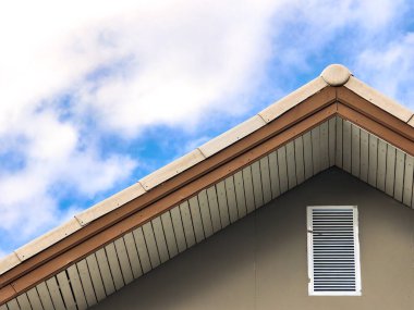 * * Modern bir evin çatısı bulutlu mavi gökyüzüne karşı, mimari detayları ve temiz çizgileri vurguluyor.