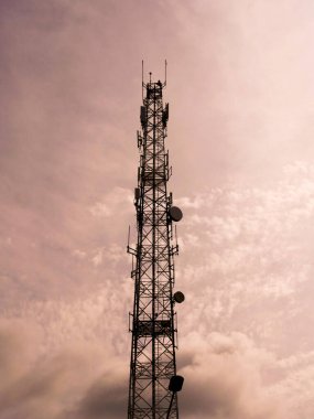 Bulutlu bir gökyüzüne kurulmuş, kırsal alanda modern teknolojiyi ve bağlantıyı sembolize eden yüksek bir iletişim yapısı..