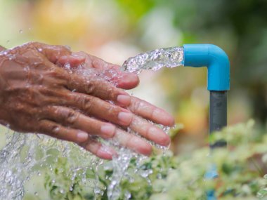 Açık havada akan musluğun altında yıkanan eller, doğal ortamdaki hijyen ve tazeliği ön plana çıkarıyor..