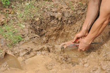 Eller su sızdıran boruları çamurdaki kerpetenle tamir eder. 