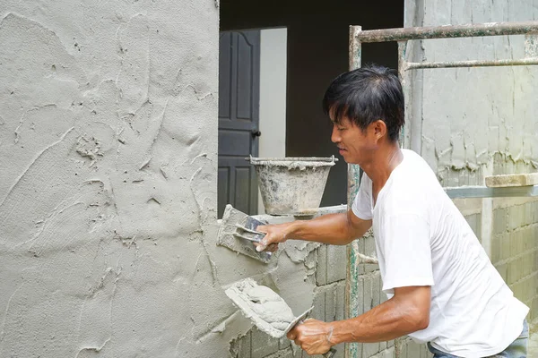 an middle age asian man looks happy, sweating while plastering cement wall at home like a hobby, selective focus