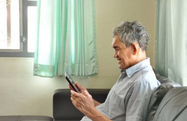 Oturma odasındaki koltukta dinlenen yaşlı bir adam tablet mutluluk kullanıyor. Seçici bir odaklanma.