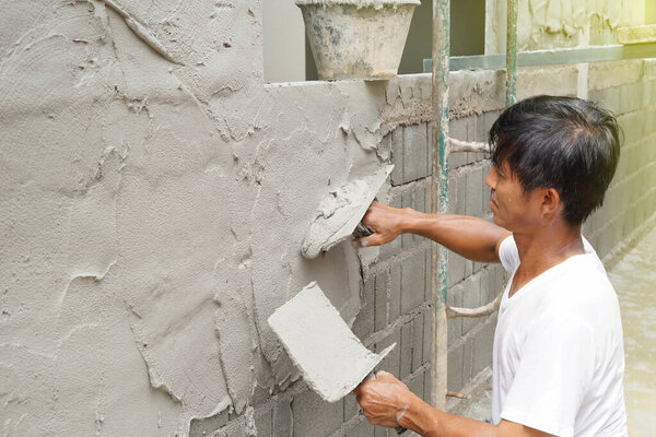 азиатский мужчина средних лет выглядит счастливым, потея в то время как штукатурка цементной стены дома, как хобби, избирательный фокус                                                                                         