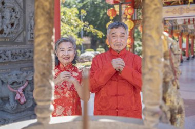 Cheongsam 'daki Asyalı kıdemli çift Çin tapınağındaki tütsü ocağında dua ediyor ve ibadet ediyor. Çin Yeni Yıl Festivali konsepti.