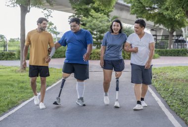 Şehir parkında spor kıyafetleriyle spor yapan bir grup insan. Protez bacaklı insanlar akşam güneşinde antrenman yaparken arkadaşlarıyla yürüyüp konuşmaktan zevk alıyorlar. 