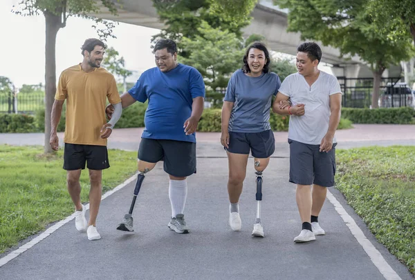 Şehir parkında spor kıyafetleriyle spor yapan bir grup insan. Protez bacaklı insanlar akşam güneşinde antrenman yaparken arkadaşlarıyla yürüyüp konuşmaktan zevk alıyorlar. 