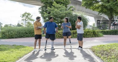 Şehir parkında spor kıyafetleriyle spor yapan bir grup insan. Protez bacaklı insanlar akşam güneşinde antrenman yaparken arkadaşlarıyla yürüyüp konuşmaktan zevk alıyorlar. 