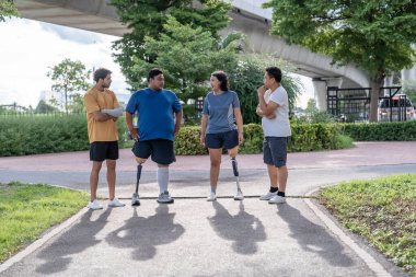 Şehir parkında spor kıyafetleriyle spor yapan bir grup insan. Protez bacaklı insanlar akşam güneşinde antrenman yaparken arkadaşlarıyla yürüyüp konuşmaktan zevk alıyorlar. 