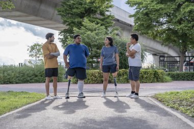 Şehir parkında spor kıyafetleriyle spor yapan bir grup insan. Protez bacaklı insanlar akşam güneşinde antrenman yaparken arkadaşlarıyla yürüyüp konuşmaktan zevk alıyorlar. 