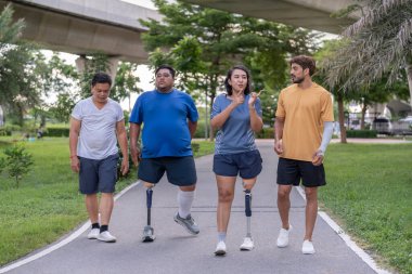 Şehir parkında spor kıyafetleriyle spor yapan bir grup insan. Protez bacaklı insanlar akşam güneşinde antrenman yaparken arkadaşlarıyla yürüyüp konuşmaktan zevk alıyorlar. 