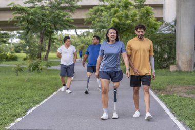 Şehir parkında spor kıyafetleriyle spor yapan bir grup insan. Protez bacaklı insanlar akşam güneşinde antrenman yaparken arkadaşlarıyla yürüyüp konuşmaktan zevk alıyorlar. 