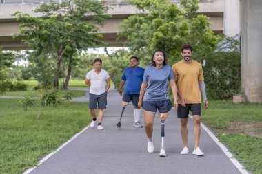 Şehir parkında spor kıyafetleriyle spor yapan bir grup insan. Protez bacaklı insanlar akşam güneşinde antrenman yaparken arkadaşlarıyla yürüyüp konuşmaktan zevk alıyorlar. 