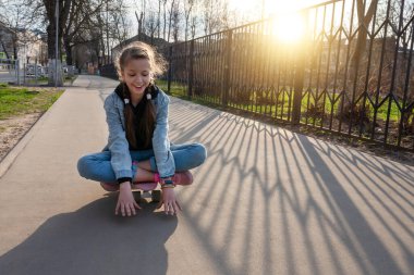 Kot pantolonlu ve pembe ayakkabılı hoş bir kız şehirde paten kayarak geziyor. Uluslararası Kaykay Günü. Spor ve Geliştirme Konsepti