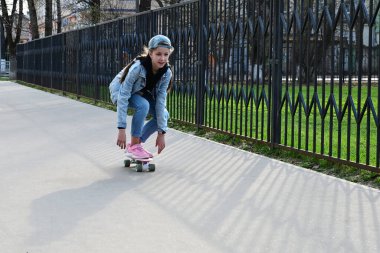 Kot pantolonlu ve pembe ayakkabılı hoş bir kız şehirde paten kayarak geziyor. Uluslararası Kaykay Günü. Spor ve Geliştirme Konsepti