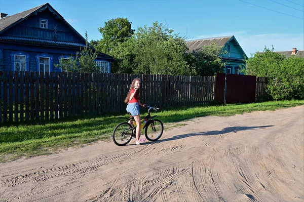 金髪の長髪の美しい10代の女の子が晴れた日に夏の村の通りを自転車で走ることを学んでいます アクティブなレクリエーションとスポーツの概念 — ストック写真