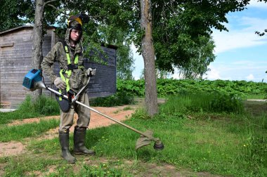 Elinde çim biçme makinesiyle özel korumalı giysiler içinde çalışan işçiler çim biçiyor. Bahçıvan çimleri biçme makinesi, çim biçme makinesi ya da çim biçme makinesi ile keser. Bahçe bakımı
