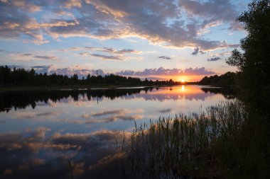 Güzel yaz günbatımı ve nehrin üzerindeki renkli gökyüzü. Bulutlar sakin suya yansıyor. Bu dünyada güzellik