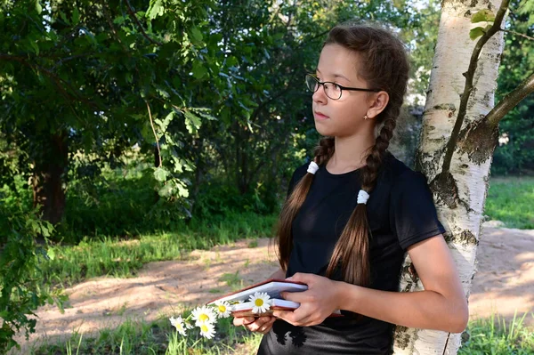 夏の公園で眼鏡をかけた可愛い10代の女の子が木に寄りかかって本を読んでる 訓練と教育の概念 学校に戻る — ストック写真