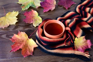 Sonbahar kompozisyonu. Bir fincan çay ve ahşap masada renkli akçaağaç yapraklarıyla örülmüş sıcak bir eşarp. Sonbahar kavramı, ev konforu ve sıcaklık