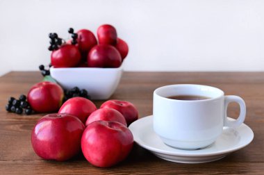 Sonbahar kompozisyonu kırmızı elmalar ve ahşap masa üzerinde duran boğuk çilek ve beyaz fincan çay. Sonbahar kavramı, ev konforu ve sıcaklık. Boşluğu kopyala