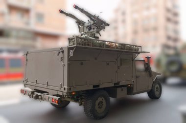 Bir askeri araç, monte edilmiş bir füze fırlatma sistemini gösteren kentsel bir ortamda konumlandırıldı. Bu sahne, şehir mimarisinin ortasında gün ışığında askeri hazırlığı yakalar..