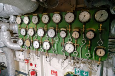 Bir geminin makine dairesindeki yeşil bir panele çok sayıda basınç göstergesi monte edilir. Ölçüler, güvenli işlemler için gerekli olan çeşitli basınç seviyelerini izler.