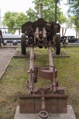 Eski bir topçu silahı askeri bir parka yerleştirildi. Paslı metal ve yıpranmış tekerlekler yeşil ve diğer askeri ekipmanlarla çevrili yaşını vurguluyor..