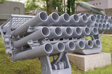 Bir askeri füze fırlatıcısı açık hava müzesinde sergileniyor. Ağaçlar ve diğer teçhizatlarla çevrelenmiş olan tesiste, eski çağlardan kalma silahlar sergileniyor ve askeri teknoloji gelişmeleri temsil ediyor..