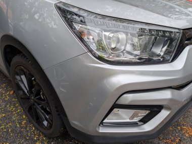 Canlı yaprakları olan ağaçlarla çevrili bir yolda gümüş renkli bir SUV park halinde. Aracın şık farları ve siyah alaşımlı tekerlekleri olan parlak bir tasarımı var..