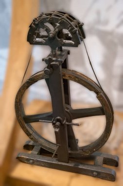 Kaliteli bir dönen tekerlek, ahşap yapısını ve karmaşık tasarımını sergileyerek bir müzede belirgin bir şekilde duruyor. Belgede, tekstil üretiminde daha önceki zamanların zanaatkarlığının altı çiziliyor.