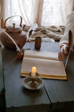 Bir insan, mum, çömlek ve mürekkep kabı da dahil olmak üzere antika eşyalarla çevrili boş bir sayfaya tüy kalemle yazar. Yumuşak ışık bir pencereden süzülür.