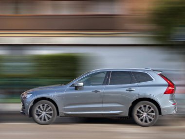 Parlak gümüş renkli bir SUV öğleden sonra bir şehir caddesi boyunca hızla ilerliyor. Hareket, dükkanları ve yeşillikleri geçerken güçlü tasarımı ve performansını vurgulayan bir bulanıklık yaratıyor..