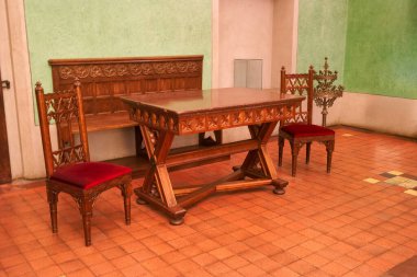 Konforlu bir odada iki süslü sandalyeyle çevrili iyi hazırlanmış ahşap bir masa bulunur. Duvarlar yumuşak yeşil bir renge boyanır. Ayak altında desenli fayanslarla sıcak bir atmosfer yaratır..