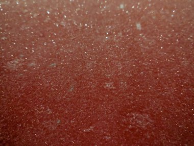 Canlı kırmızı bir yüzeye yakın bir bakış yumuşak ışık altında parlar, küçük parlak parçacıklarla dolu eşsiz bir doku sergiler. Sahne sıcak ve davetkar bir atmosferi çağrıştırıyor..