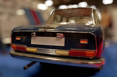 Klasik bir araba sergi salonunda, katılımcıların dikkatini çeken bir şekilde duruyor. Araç parlak krom detaylara ve renkli görüntülerle çevrili parlak mavi bir vücuda sahip..