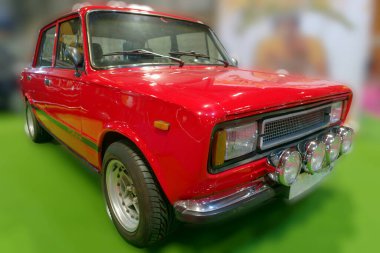 Kongre merkezinin içine park etmiş dört parlak ışığı olan kırmızı bir araba. İç mekan, aracı yakından inceleyen ve fotoğraf çeken insanlarla dolu..