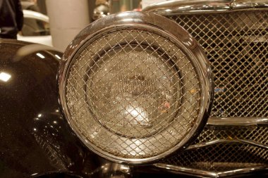 Eski bir arabanın farına yakından bakınca tel örgü örülüyor. Sergi, akşam saatlerinde çeşitli klasik arabaların bulunduğu bir otomotiv sergisinde yer alıyor..