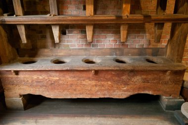 Tahtadan yapılan bu bank birkaç dairesel delik içeriyor ve tuğla bir duvara dayanıyor. Geleneksel işçiliğin benzersiz tasarımı ve hikaye geçmişini vurguluyor..