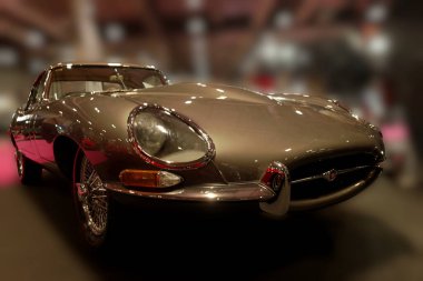 Eski bir araba bir otomobil fuarında sergilenir. Dekorun parlak ışıkları var ve arka planda birçok insan görülebilir. Arabanın parlak bir dış görünüşü var ve vitrinde duruyor..