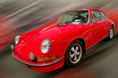 Bir araba fuarında klasik kırmızı bir spor araba pistte hızlanır. Şehir ışıkları hızını ve tasarımını sergiledikçe canlı bir zemin oluşturur..