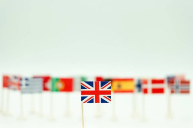 Birçok başka ülke bayraklarının önünde küçük bir Birleşik Krallık bayrağı duruyor. Bayraklar düz bir arkaplana karşı sıraya dizilmiştir. Bu sahnede farklı uluslardan bayraklar var..