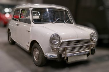 Beyaz bir antika araba bir müze alanında sergilenir. Araç yuvarlak özellikli eşsiz bir tasarım gösteriyor. Yumuşak ışıklandırma klasik şeklini ve şeklini vurgular. Ziyaretçiler bölgeyi keşfediyor.