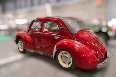Klasik kırmızı bir araba bir araba sergisinde büyük bir kapalı alanda sergileniyor. Klasik bir tasarımı var ve ziyaretçilerin görmesi için diğer araçların arasına park edilmiş..
